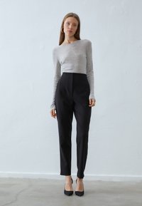 Maglietta grigia a maniche lunghe abbinata a pantaloni neri a vita alta. Vestibilità elegante e tessuto morbido. Tacchi a punta neri completano l'outfit.