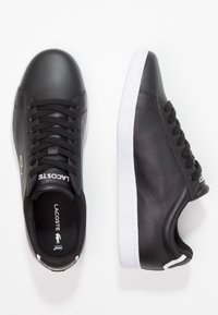 Svarta lädersneakers med vita gummisålar, utrustade med svarta snören, sydda detaljer och en logo på sidan. Enkelt design och rundad tå.