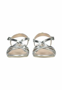 Sandali piatti in metallo argentato con cinturini incrociati e fibbie alla caviglia, visti frontalmente su sfondo bianco.