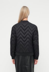 Zwarte gewatteerde jas met chevron-quilting, ribgebreide manchetten en tailleband, met een ronde hals en een zachte textuur.