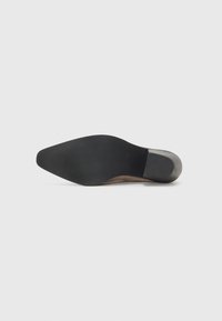 Scarpa con tacco alto e punta affusolata, in suede color cammello, con suola in gomma nera. Caratterizzata da un design elegante e una struttura minimalista.