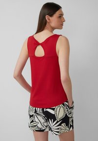 Rode mouwloze top met een geknoopte uitsnijding op de rug; gecombineerd met zwarte shorts met een wit bladerenpatroon. Gladde katoenen textuur.