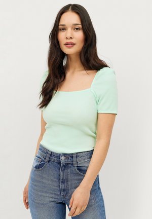 Mintgroene geribde top met korte pofmouwen en een vierkante halslijn, gecombineerd met lichtblauwe high-waisted jeans.