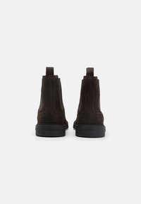 Botine din suede maro, cu detalii perforate și talpă din cauciuc negru. Au elemente pentru tragere la spate pentru a fi ușor de încălțat.