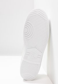 Semelle de chaussure en caoutchouc blanc avec un motif texturé de prise et des accents circulaires. Taille 37 imprimée sur le caoutchouc. Fond blanc uni.