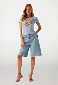Svetlo modra majica s trikotnim grafičnim vzorcem in okraski, kombinirana s svetlim bermudskim jeans kratkimi hlačami z raztrganim robom. Rjave sandale z visokimi petami.