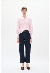 Lys rosa bluse med puffede ærmer og blonde detaljer, parret med mørke højtaljede jeans og flade sko med leopardprint.
