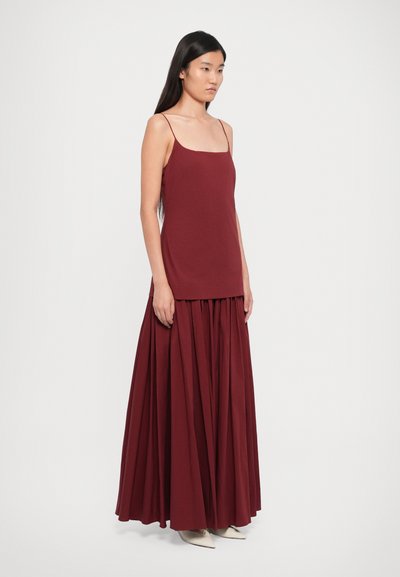 Burgundy sleeveless top paired with a matching full-length pleated skirt, made from a smooth fabric with subtle draping.