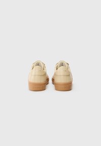 Sneakers beige con tomaia in pelle liscia e punta rotonda. Dotati di suola in gomma color tan e logo del brand impresso sul tallone e sulla suola.