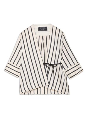 Blouse portefeuille blanche à rayures noires verticales, manches trois-quarts, avec une fine ceinture noire à nouer à la taille.