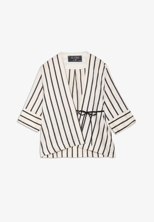 Blouse portefeuille blanche à rayures noires verticales, manches trois-quarts, avec une fine ceinture noire à nouer à la taille.