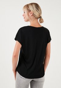 Zwarte T-shirt met een relaxte pasvorm, korte opgerolde mouwen, ronde halslijn en een rechte snit. Glad stof met minimale details op de achterkant.