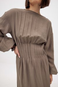 Abito khaki realizzato in tessuto testurizzato. Presenta pieghe raccolte in vita e maniche ampie. Finitura liscia con una leggera lucentezza.