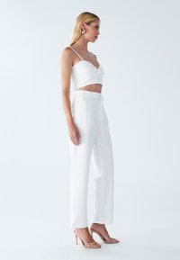 Biały krótki top z skręconym przodem, w zestawieniu z luźnymi białymi spodniami. Błyszczące złote dodatki i beżowe sandały na obcasie dopełniają całość.