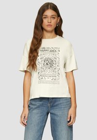 Crème-kleurige oversized t-shirt met een zwarte grafische print met tekst en bloemdessins. Korte mouwen en een relaxte pasvorm. Draagt bij blauwe jeans.