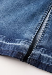 Denimtyg i en bleknad blå färg med dragkedjestängning och kontrasterande gula sömmar längs kanterna och sömdetaljer.