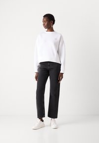 White cotton sweatshirt with a round neck and dropped shoulders, paired with dark gray wide-leg jeans and white sneakers. Simple design, no patterns.