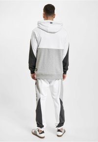 Sweatshirt à capuche et pantalons de jogging en blanc, gris et gris foncé. Présente un design coloré, des poignets côtelés et des accents de marque sur le pantalon.