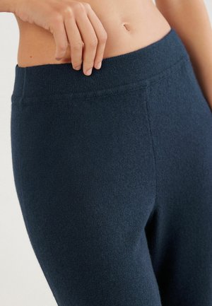 Leggings en tricot bleu marine avec une large taille en tissu et une texture lisse et douce. Un gros plan montre le détail de la taille et du tissu.