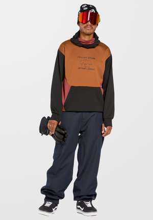 Hooded sweatshirt in brown, black, and maroon with graphic print. Loose-fitting navy pants and black gloves. Reflective ski goggles worn.