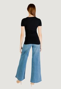 T-shirt nera attillata abbinata a jeans larghi di colore blu chiaro, con una texture morbida e un design informale, vista da dietro.