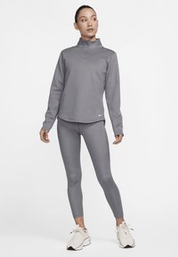 Sivi sportski pulover s ovratnikom na pola zatvarača, uparen s odgovarajućim tajicama i svijetlim tenisicama. Glatka tekstura, minimalistički dizajn, brendirani logo.