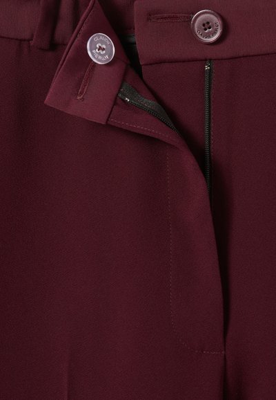 Pantaloni bordeaux con una texture liscia, dotati di chiusura con bottone e zip, e dettagli di cucitura visibili vicino alla vita.