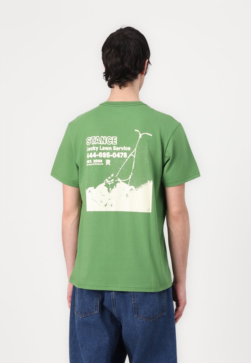 T-shirt de algodão verde com uma ilustração de um corta-relva nas costas, com texto branco para "Serviço de Cortar Relva Sortudo" e detalhes de contacto.