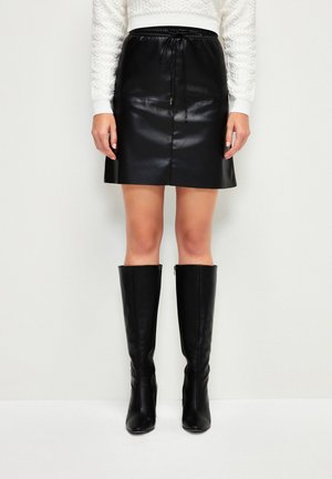 Falda de piel sintética negra con cintura ajustable, corte recto y textura suave; combinada con botas altas de cuero negro.