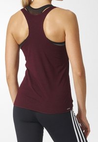 Burgundy ärmlös tank top med racerback-design, tillverkad av mjukt tyg, lagd över en svart sport-bh, kombinerat med svarta leggings.
