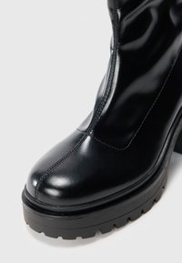 Bottine en cuir noir à plateforme épaisse avec coutures frontales et semelle crantée sur fond clair.