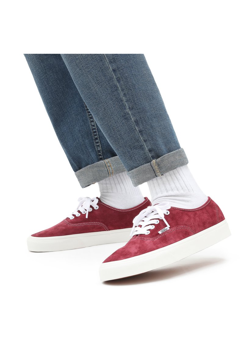 Zapatillas de ante rojo con cordones blancos, suela de goma y puntera reforzada. Combinadas con jeans de mezclilla azul doblados y calcetines blancos.