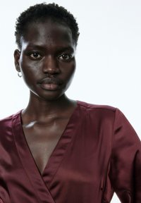 Bordeaux-satin Kleid mit tiefem V-Ausschnitt, glatter Textur und kurzen Ärmeln. Minimale Details und eine leicht lockere Passform an den Schultern.