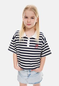 Polo de rayas azul marino y blanco de manga corta con cuello blanco y bordado de estrella de mar roja, combinado con una falda de mezclilla clara.