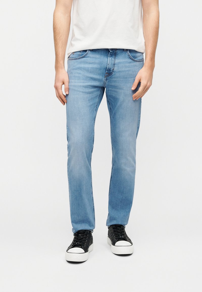 Ανοιχτό μπλε τζιν παντελόνι με ευθεία γραμμή, ραφές για διακόσμηση και πλαϊνές τσέπες, σε συνδυασμό με μαύρα αθλητικά παπούτσια με λευκές σόλες.