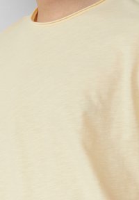 Lichtgele t-shirt met een zachte, gladde textuur en een ronde halslijn. De stof lijkt lichtjes getextureerd met een subtiel heatherpatroon.