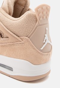 Beige suede sneaker with a textured upper, white midsole, and a rubber heel tab featuring a Jumpman logo.