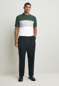 Zöld, szürke és fehér színű, színblokkos galléros póló, pamut keverék, rövid ujjú. Fekete nadrággal és fényes fekete cipővel párosítva.