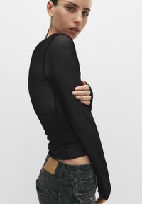 Cămașă neagră cu mânecă lungă, cu model texturat de puncte, având un design cu pliuri pe laterale. Asortată cu blugi din denim decolorat.