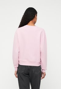 Sweatshirt roz deschis cu guler rotund, manșete și tiv ribbate. Materialul pare moale și are o croială confortabilă. Purtați-l cu pantaloni gri.