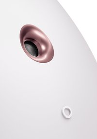 Surface d'appareil blanc avec une ouverture de haut-parleur ronde en or rose et un petit port circulaire blanc, offrant une texture lisse et un design minimaliste.