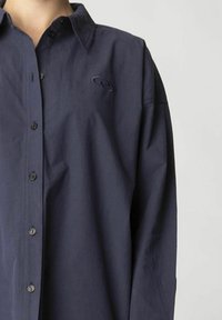 Marineblaues Hemd mit Knöpfen aus leichtem Stoff, das einen Kentkragen, lange Ärmel und ein kleines Logo auf der Brust hat.
