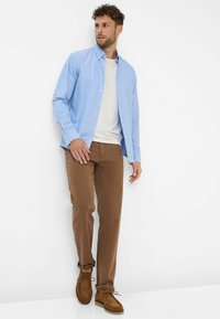 Camicia azzurra chiara button-up sopra una T-shirt bianca, abbinata a pantaloni marroni e scarpe in suede marroni. Caratterizzata da una tasca sul petto e vestibilità casual.