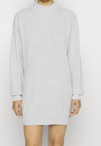 Ljusgrå stickad klänning med hög hals, långa ärmar samt ribbade manschetter och nederkant. Mjuk textur och avslappnad passform.