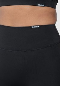 Černé sportovní legíny s vysokým pasem, vyrobené z hladkého, elastického materiálu. Obsahují dvě malé štítky SMILODOX.