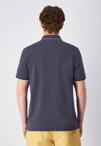 Marineblaues Polohemd mit weißen Kragenbesätzen, kurzen Ärmeln und geradem Saum. Hergestellt aus glattem Stoff, entworfen für eine lockere Passform.