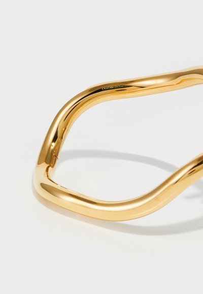 Brățară din metal aurit cu un design neted și curbat; dispune de margini rotunjite și o finisare reflexivă, evidențiind forma sa elegantă și minimalistă.
