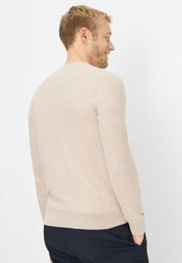 Beiger Strickpullover mit Rundhalsausschnitt, langen Ärmeln und gerippten Bündchen. Der Stoff hat ein strukturiertes Muster und eine leichte Oberfläche.