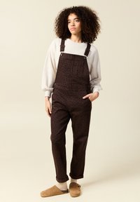 Bruna leopardmönstrade overaller med justerbara axelremmar och framficka, tillsammans med en ljusgrå sweatshirt och bruna tofflor, med upprullade ärmslut.