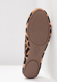 Semelle d'une chaussure à imprimé léopard avec un fond en caoutchouc marron à motifs, logo "Dune London" et taille 37 sur une surface blanche et un coin de mur.